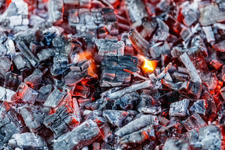 A pile of wood that has been burned, with the charred remains of the wood still glowing red. The wood is covered in ash and has a rough, jagged texture. Concept of destruction and decayの写真素材