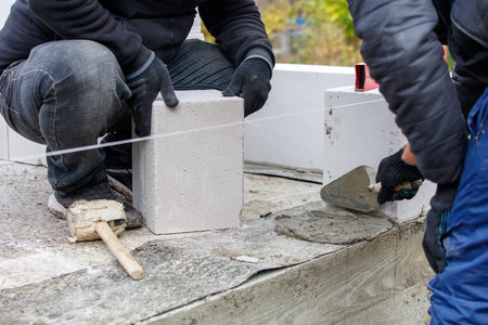 Two men are laying bricks on a wall. One of them is using a trowel to spread mortarの写真素材