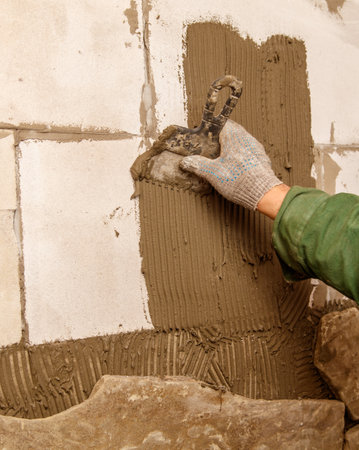 A man is using a trowel to apply a brown substance to a wall. Concept of manual labor and craftsmanship, as the man carefully spreads the material to create a smooth and even surfaceの写真素材