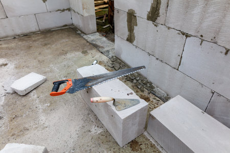 A trowel and a hammer are placed on top of a cement block. The trowel is positioned to the left of the hammer, and both tools are resting on the blockの写真素材
