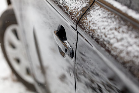 A car door is covered in snow and ice. The door is black and the snow is whiteの写真素材