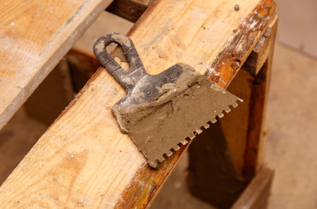 A trowel with a bit of cement on it is sitting on a wooden surface. The trowel is old and worn, and the cement is chipped and uneven. The scene gives off a sense of wear and tearの写真素材