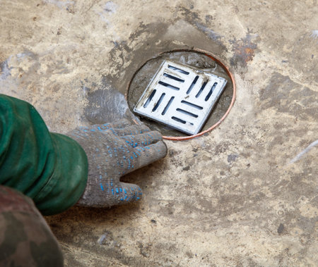A person is working on a drain with a metal grate. The person is wearing a green jacket and glovesの写真素材