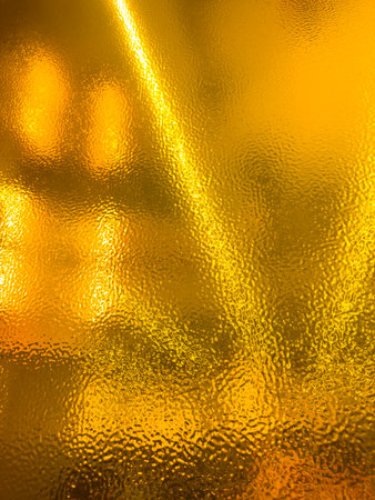 A blurry image of a gold surface with a yellow hue. The surface appears to be a window or a piece of glass, and the image is somewhat hazyの写真素材