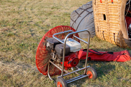 A red and white fan is placed on the grass next to a basket. The fan is positioned in the center of...
