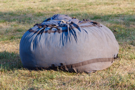A large gray bag sits on the grass. The bag is filled with ropes and other items. The scene is calm and peaceful, with the bag sitting alone in the grassの写真素材