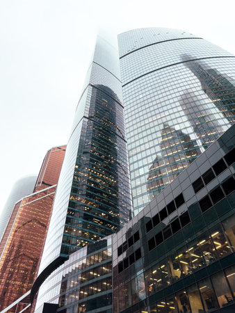A city skyline with tall buildings and a cloudy sky. The buildings are made of glass and have a...
