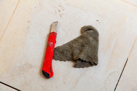A pair of scissors and a piece of cloth are laying on a tile floor. The scissors are red and the cloth is brownの写真素材