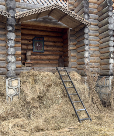 A ladder is leaning against a pile of hay. The hay is piled up against a log cabinの写真素材