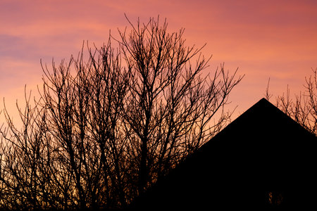 A house is silhouetted against a pink and orange sky. The house is dark and the sky is brightの写真素材