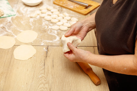 A woman is making dough on a wooden table. She is rolling out the dough with a rolling pin