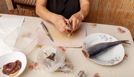 A woman is preparing food on a table with a plate of fish on it. She is using a knife to cut the fishの写真素材