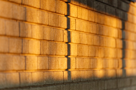 The brick wall is illuminated by the sun, casting a shadow on the ground. The warm light creates a cozy and inviting atmosphereの写真素材