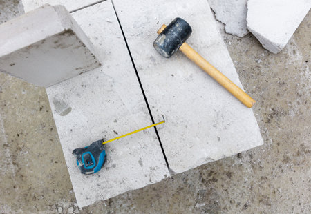 A hammer and tape measure are on a cement block. The hammer is black and the tape measure is yellow