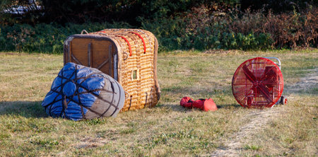 A red fan sits on the grass next to a blue bag and a wooden crate. The scene is casual and relaxed,...