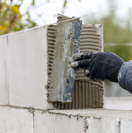 A man is using a trowel to apply cement to a wall. Concept of manual labor and hard work, as the man...
