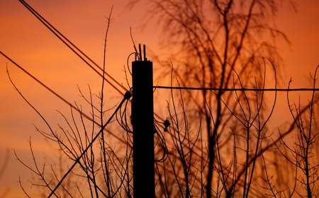 A pole with wires on it is silhouetted against a beautiful orange sky. The sky is filled with clouds...