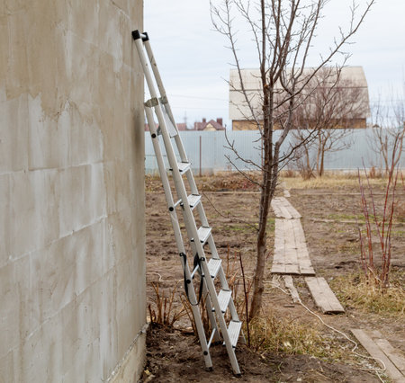 A ladder leaning against a wall with a fence in the background. The ladder is white and has six stepsの写真素材