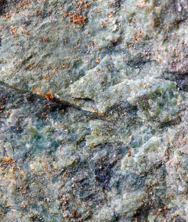 A rock with a greenish color and some brown spots. The rock is rough and has a grainy texture