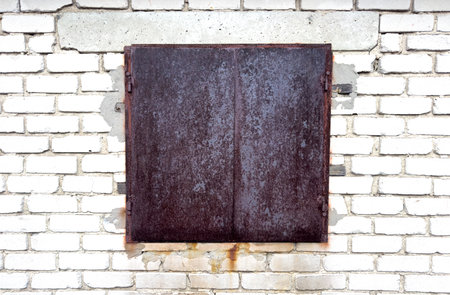A window with a metal door is on a brick wall. The door is rusted and the window is emptyの写真素材