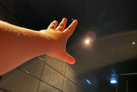 A hand is raised in the air with a light shining on it. The light is coming from a ceiling light.