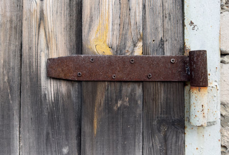 A rusty hinge on a wooden door. The hinge is old and rusted, and the door is made of wood