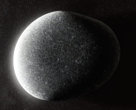 A black rock with a shiny surface. The rock is small and has a dark color. It is placed on a dark...