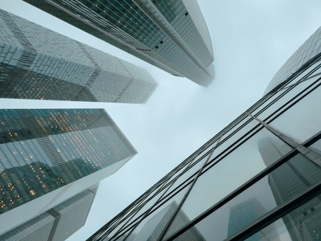 A city skyline with tall buildings and a cloudy sky. The buildings are made of glass and are very tall, with some reaching up to the clouds. The sky is overcast, giving the scene a somewhat gloomyの写真素材