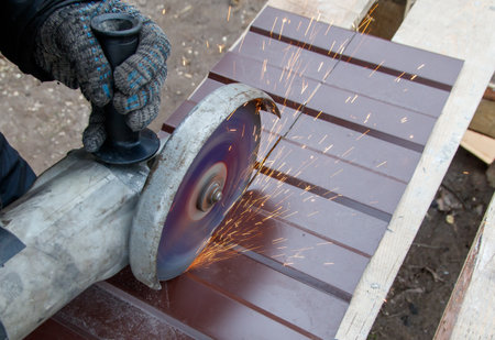 A man is using a power tool to cut a piece of wood. Concept of hard work and determination as the man focuses on his task. The sparks flying from the tool add a sense of dangerの写真素材
