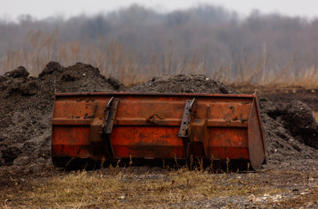 A rusty red dump truck sits in a field of dirt. The truck is old and rusted, and it is surrounded by a pile of dirt. The scene is desolate and abandoned, with no signs of life or activityの写真素材
