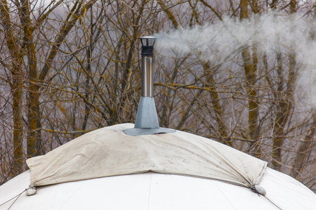 A chimney is smoking and the smoke is rising up into the sky. The chimney is on top of a roof.の写真素材
