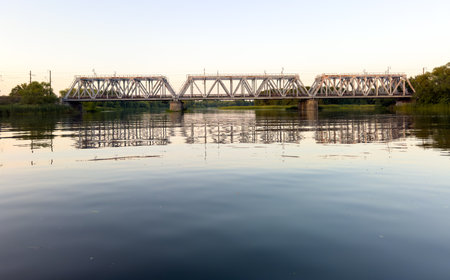 A bridge spans a river, with a reflection of the bridge in the water. The bridge is old and has a...