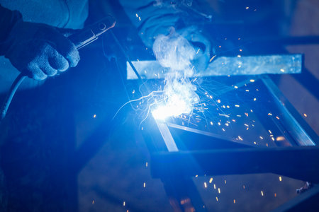 A man is welding a piece of metal with a blue flame. Concept of hard work and dedication, as the man...