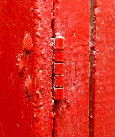 A red door with a rusty hinge. The hinge is bent and the door is slightly open. The door is old and worn, with a red paint job. Scene is somewhat melancholicの写真素材