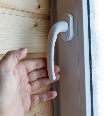 A hand is reaching for a window handle. The handle is white and has a rubber grip. The window is open, and the view outside is blurry. Concept of curiosity and explorationの写真素材