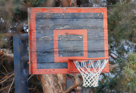 A wooden basketball hoop with a black and red net. The net is missing a few strings. The hoop is old and worn, with a black and red paint job. The image has a nostalgic and somewhat melancholic moodの写真素材