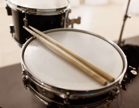 A pair of drumsticks are resting on a drum head. The drumsticks are wooden and appear to be well-used. The drum set is placed on a table, and the scene conveys a sense of creativityの写真素材