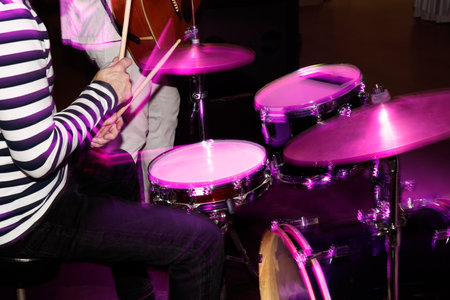 A person is playing drums with a pink drum set. The drum set is pink and has a purple rim. The person is sitting on a chair while playing the drumsの写真素材