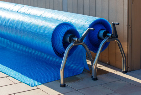 Two blue and white plastic sheets are propped up on a metal stand. The sheets are likely used for pool covers or other water-related purposes. The stand is positioned on a brick or concrete surfaceの写真素材