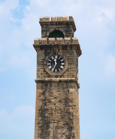 A clock tower with a clock face showing the time of 10:00. The tower is tall and made of stone. The...