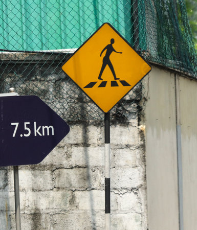 A yellow sign with a man walking on a crosswalk is on a pole next to a sign that says 7.5 kmの写真素材