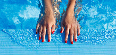 A woman's hands are in the water, with her nails painted red. Concept of relaxation and leisure, as the woman is enjoying her time in the poolの写真素材