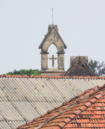A small cross is on top of a building. The building is old and has a slanted roofの写真素材