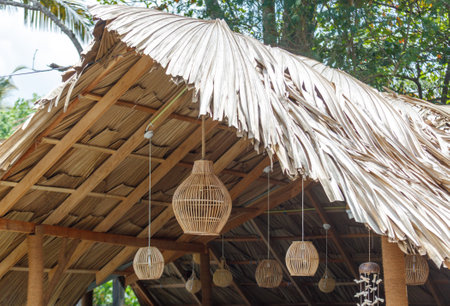 A hut with a thatched roof and hanging lanterns. The lanterns are hanging from the ceiling and are of different sizes. The hut has a rustic and cozy feel to itの写真素材