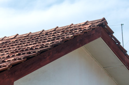 A slanted roof with a red trim and a white wall. The roof is made of tiles and the wall is made of bricks. The roof is slanted to allow rainwater to run off easilyの写真素材