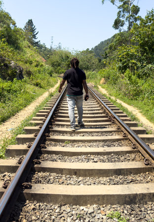 A man is walking on a train track. The train is not in motion. The train track is surrounded by trees and grassの写真素材