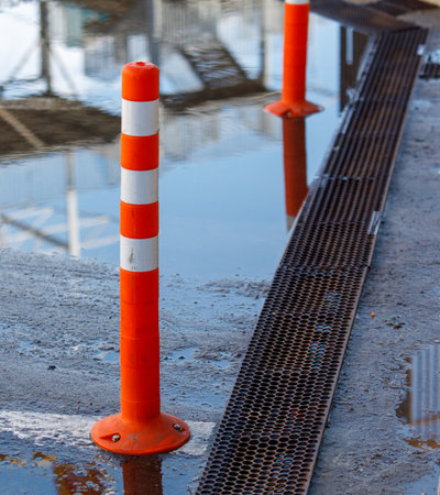 A tall orange and white pole is standing in a puddle of water. The pole is likely a traffic sign or a warning sign, as it is placed in the middle of the waterの写真素材
