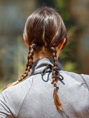 A woman with long brown hair has her hair in two braids. The braids are tied with a black ribbon