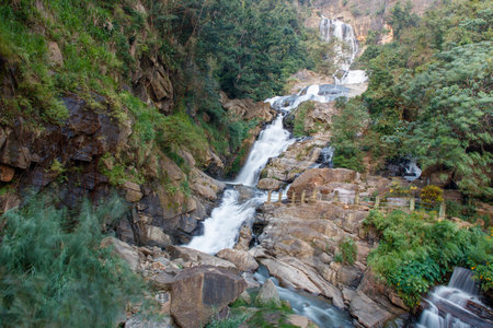 A waterfall is flowing down a rocky hillside. The water is clear and the rocks are jagged. The scene is peaceful and sereneの写真素材