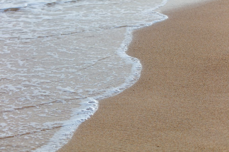 The ocean waves are crashing onto the shore, creating a beautiful and calming scene. The water is white and foamy, and the sand is a warm, golden color. Concept of peace and tranquilityの写真素材